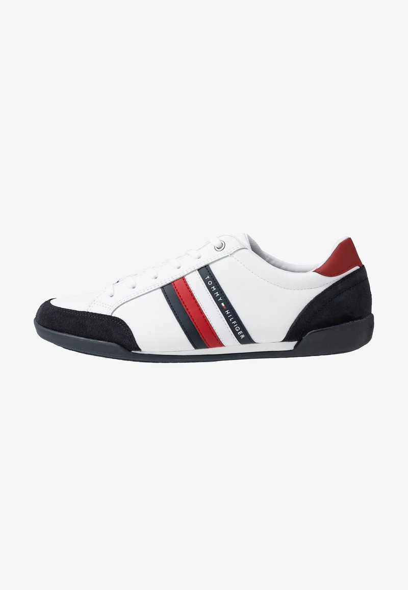 Vit låg sneakers med svarta och röda ränder, svart mocka tå och häl, samt en röd hälflik, märkt med Tommy Hilfiger-logotypen.