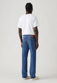 White cotton t-shirt paired with blue denim jeans. Jeans feature classic five-pocket design and brown leather patch at the back.