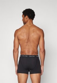 Schwarze Boxer-Shorts mit einem Calvin Klein-Logo auf einem schwarzen Bund. Der Stoff wirkt elastisch und glatt, entworfen für einen enganliegenden Look.