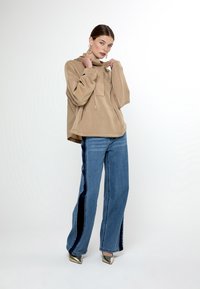 Sudadera oversized beige con cordón y bolsillo frontal. Vaqueros de luz azul con rayas laterales oscuras, de pierna ancha, combinados con tacones metálicos de punta afilada.