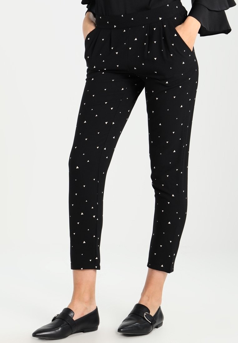 Zwarte taps toelopende broek van stretchy stof, met kleine witte driehoekpatronen, een elastische tailleband en zijzakken.