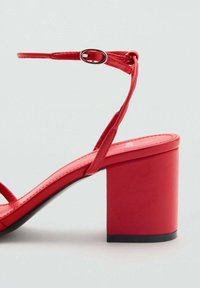 Sandal cu toc bloc roșu, având un finisaj din piele netedă, curea subțire la gleznă și un design minimalistic.