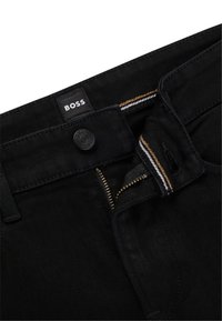 Black denim jeans featuring a zip fly and button closure, with contrasting yellow and white stitching. Logo patch on the waistband.