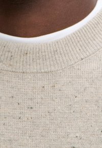 Beige Rundhals-Pullover mit strukturiertem Strick und mehrfarbigen Einsprengseln. Der Kragen hat ein kontrastierendes weißes Innenfutter.