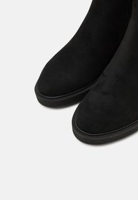 Botine negre din suede cu o textură netedă, vârf ascuțit și talpă joasă din cauciuc, având detaliu cu fermoar pe laterale.