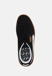 Baskets en daim noir avec une bande latérale blanche et un logo doré, dotées d'une semelle intérieure texturée noire et blanche et d'une semelle extérieure en caoutchouc marron.