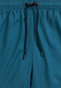 Turkusowe kąpielówki o fakturze z elastycznym paskiem w talii, z czarnym sznurkiem do regulacji, ozdobione prążkowanym wzorem.