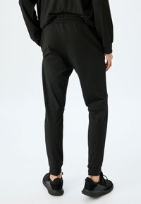 Zwarte sportlegging met een elastische tailleband, taps toelopende benen en een aansluitend ontwerp. Gecombineerd met zwarte sneakers, die een gladde textuur en stiksels tonen.