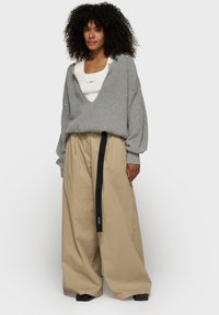 Pull gris surdimensionné avec un décolleté en V profond et une texture côtelée, associé à un pantalon beige à larges jambes mettant en avant une ceinture noire.