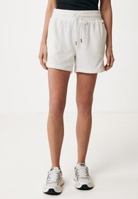 Shorts bianchi in cotone con finitura testurizzata, vita elastica e cordino. Presentano orlo ripiegato e tasche laterali. Indossati con sneakers chiare.