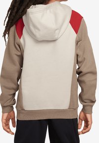 Hoodie med en krämfärgad rygg, bruna ärmar och en röd axeldetalj. Tillverkad av mjukt tyg med en avslappnad passform.