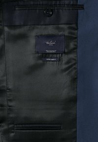 Doublure en satin noir d'une veste bleue sur mesure avec des étiquettes indiquant "tailored MNG" et "super slim fit" à l'intérieur d'une poche intérieure.