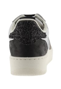 Sneaker bianco con tacco in camoscio nero testurizzato e accenti neri scintillanti. Presenta una suola in gomma e un design liscio ed elegante.