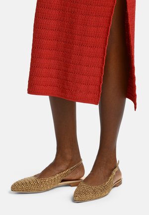 Rudos odos kojos, avinčios auksinius austus atvirus batelius su dirželiais, derinamos su raudona tekstūruota midi sijonu su šonine skeltimi.