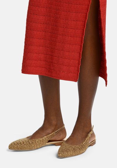 Brunlige ben iført gyldne flettede slingback-flats kombineret med en rød tekstureret midi-nederdel med sideslids.