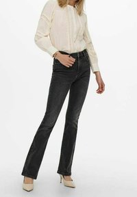 Black flared jeans with a high waist, a smooth textured fabric, paired with a light cream blouse featuring lace detailing and buttons.