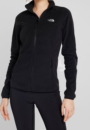 Černá fleecová bunda na zip s vysokým límcem, zipovými kapsami na bocích a logem The North Face na levé straně hrudi, nošená s černými kalhotami.