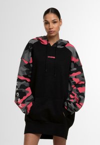 Černé šaty se sweatshirtovým vzhledem, s růžovou a šedou maskáčovou kapucí a rukávy. Obsahují přední kapsu a značkové logo v růžové barvě na hrudi.