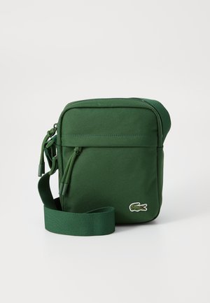 Borsa a tracolla verde in tessuto con chiusura a zip, tracolla regolabile e piccolo logo ricamato sul davanti. Texture morbida e forma rettangolare.