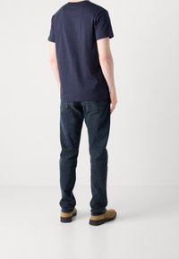 Marineblå bomulds T-shirt, blå denim jeans og brune sko. T-shirten har rund hals og korte ærmer; jeansene er slim-fit med baglommer.