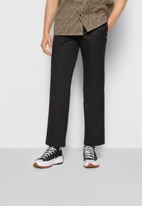 Czarne spodnie o prostym kroju, w połączeniu z czarno-białymi sneakersami. Góra z brązowym wzorem w cętki. Minimalistyczny design.