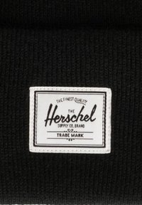 Tessuto nero lavorato a maglia con un'etichetta rettangolare bianca con la scritta "Herschel Supply Co." e dettagli decorativi sul bordo.