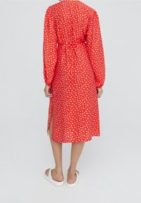 Vestido rojo con patrón floral blanco, de mangas largas, con cinturón a la cintura, aberturas laterales, hecho de tela ligera, que llega hasta la mitad de la pantorrilla.