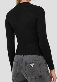 Schwarzes, geripptes Langarmoberteil mit enganliegender Silhouette und hohem Kragen, kombiniert mit grauen Jeans, die eine dreieckige Logotasche aufweisen.