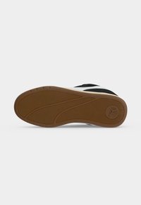 Semelle extérieure d'une basket noir et blanc avec une semelle en caoutchouc marron, une bande de roulement texturée et un logo circulaire près du talon sur fond blanc.