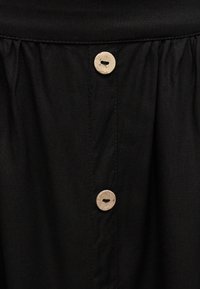 Μαύρο ύφασμα με δύο μπεζ στρογγυλά κουμπιά τοποθετημένα κάθετα κατά μήκος μιας ραμμένης ραφής στο κέντρο.