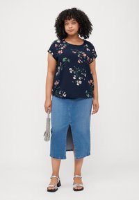 Navy floral top with short sleeves and a round neckline, paired with a knee-length denim skirt featuring a front slit. Silver sandals complete the look.