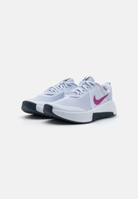 Hvite joggesko med mesh-overdel, lilla Nike-svosh, grå detaljer og teksturert svart såle. Snører og minimal merkevareprofil inkludert.