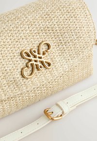 Beige színű, fonott szalma kézitáska aranyszínű fém logó díszítéssel. Fehér bőr pánt arany csattal. Texturált felület.