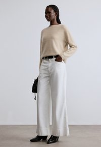 Beżowy, miękki sweter i szerokie białe spodnie. Czarny pasek, szpiczaste wysokie buty na obcasie oraz mała czarna torebka. Prosty, nowoczesny design, neutralne kolory.