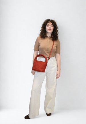 Bluza bej cu nasturi, pantaloni albi cu picioare largi și o geantă mică roșie țesută, cu mâner superior, purtată încrucișat pe corp. Pantofii maro completează ținuta.