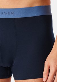Boxer briefs blu navy con elastico leggero blu chiaro. Il tessuto appare liscio; logo integrato in modo discreto nel design dell'elastico.