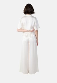 Ivory zijden shirt en wijde broekset, met korte mouwen, elastische taille en een gladde textuur. Van achter bekeken.