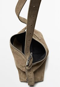 Borsa in suede khaki con tracolla regolabile, zip argentata e interno nero. Presenta una forma arrotondata e cuciture dettagliate.