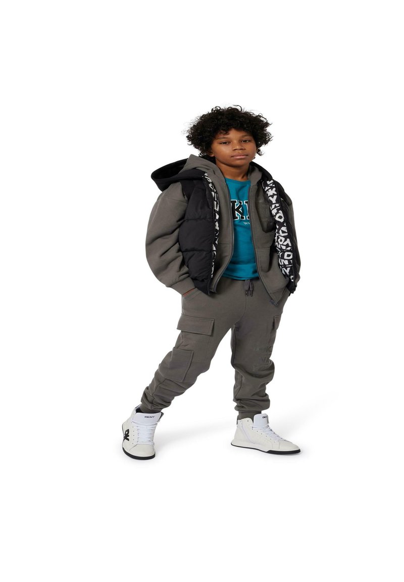 Grijze pufferjack met zwarte accenten, turquoise sweatshirt, bijpassende grijze joggers en witte high-top sneakers met zwarte logo's.