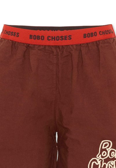 Pantaloni in tessuto marrone con una vita elastica rossa caratterizzata dalla ripetizione del testo nero "BOBO CHOSES" e parte di un logo bianco sulla gamba destra.