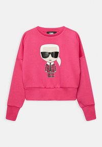 Rosa croppad sweatshirt i mjukt tyg med en tecknad grafik av en figur med solglasögon och mönstrad kostymdesign på framsidan.