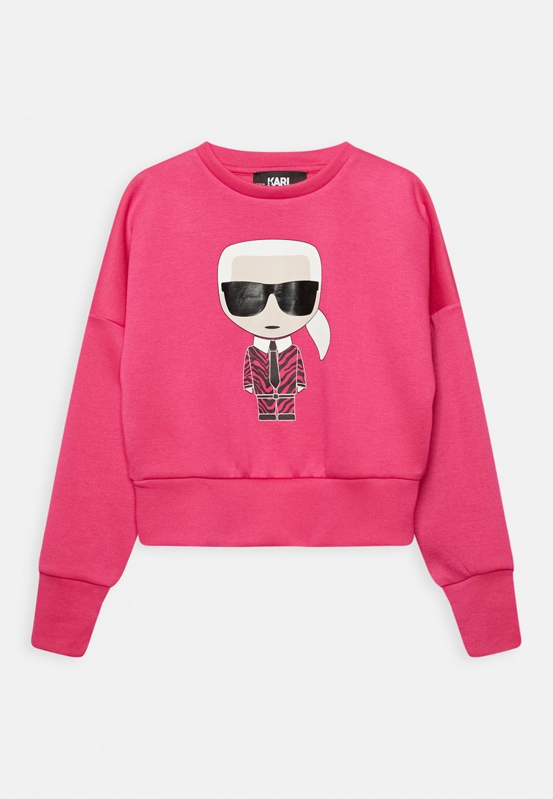 Rosa croppad sweatshirt i mjukt tyg med en tecknad grafik av en figur med solglasögon och mönstrad kostymdesign på framsidan.