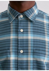 Koszula flanelowa zapinana na guziki, z wzorem w niebiesko-czarną i białą kratę, klasycznym kołnierzykiem oraz jasnymi guzikami.
