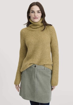 Chunky mosterdkleurige coltrui met ribbelstructuur, gecombineerd met een lichtgroene corduroy rok met een knoop en verticale strepen.
