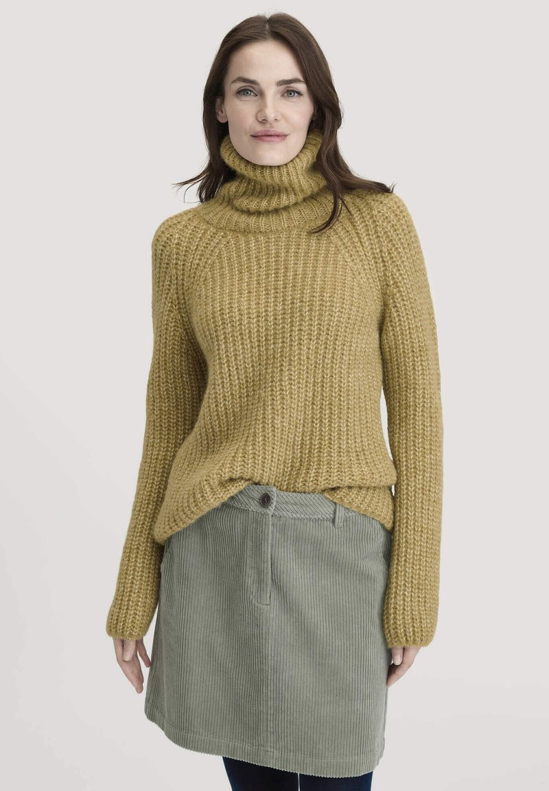 Fülliger Senf-turtleneck Pullover mit gerippter Textur, kombiniert mit einem hellgrünen Cordrock, der einen Knopf und vertikale Streifen aufweist.