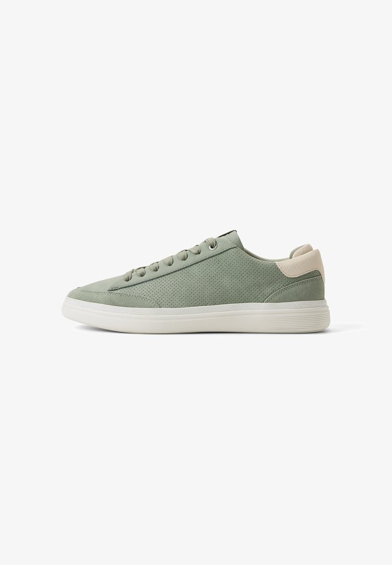 Zapatilla deportiva baja de color verde claro con parte superior de ante perforado, lengüeta beige en el talón, suela de goma blanca y cierre de cordones, mostrada desde el lado exterior.