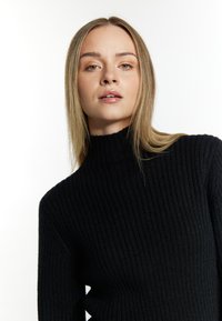 Maglione nero a collo alto con costo a coste, caratterizzato da un tessuto testurizzato e una silhouette aderente. Design minimalista senza decorazioni.