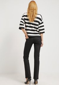 Camiseta de rayas en blanco y negro de corte oversized con mangas de tres cuartos, combinada con jeans ajustados negros y zapatos de tacón alto, vista desde la parte de atrás.