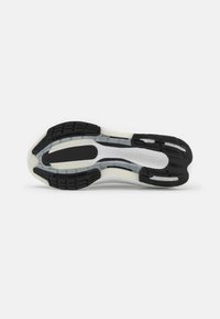 Sole di sneaker in bianco e nero con motivi di trazione in gomma testurizzata e sezioni trasparenti lisce, con "LIGHTBOOST" impresso sul lato.