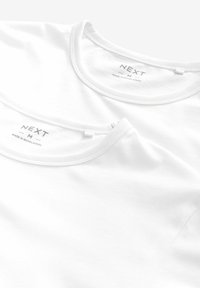 Du du baltos medvilninės T-shirt'ų, dėvimos viena ant kitos, su apvaliais iškirpimais ir mažais "NEXT" etiketėmis vidinėje iškirpimo pusėje. Lygi textura, be matomų raštų.